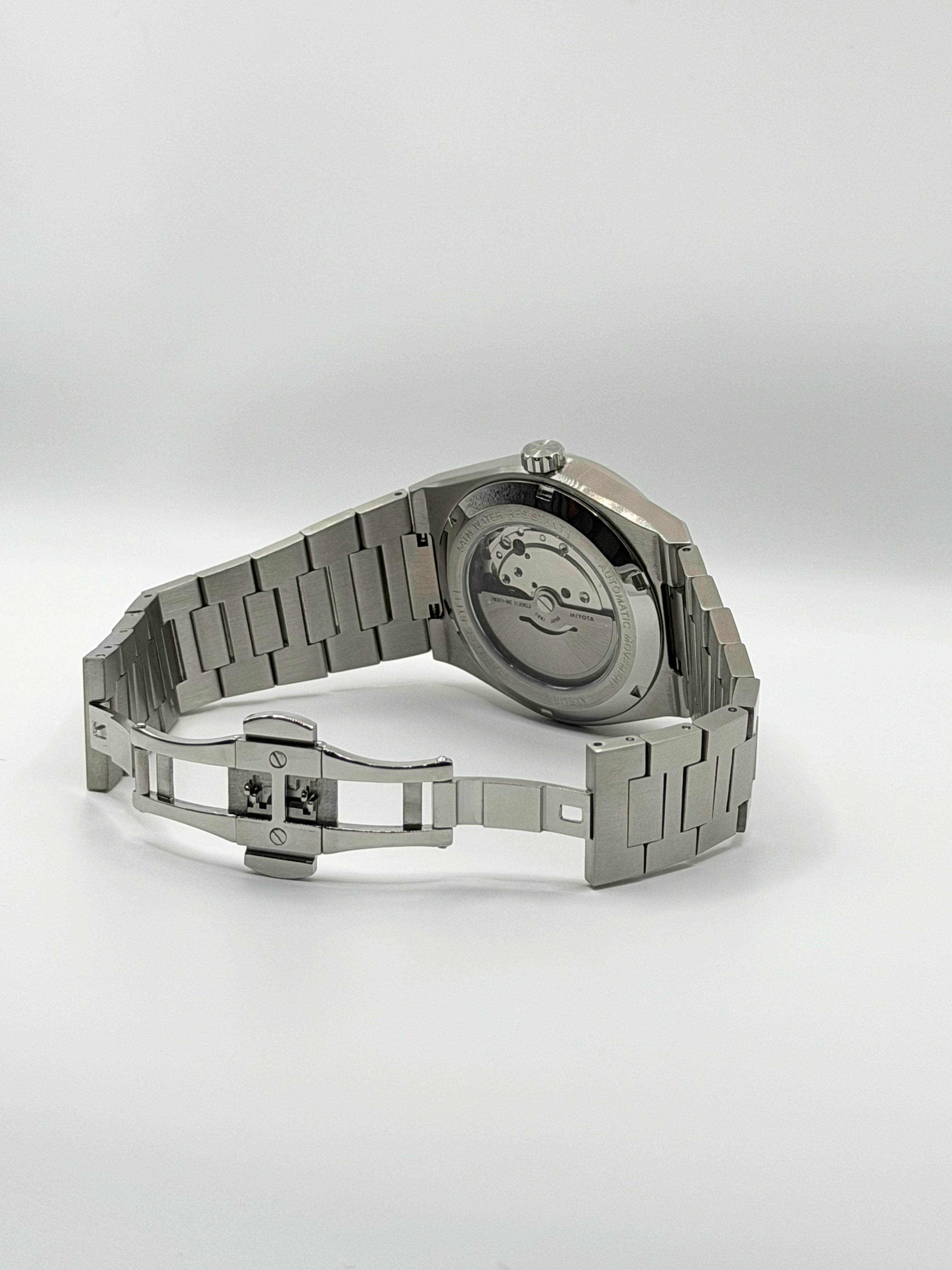 A silver stainless steel automatic watch with a metal link butterfly integrated bracelet, shown from the back to display the transparent case and internal mechanical movement.